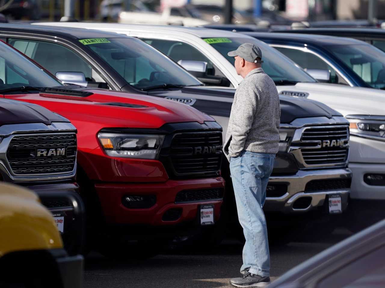 A man wearing a hat looks at cars on a dealership lot.