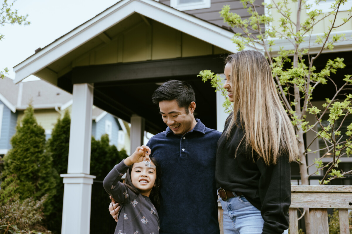 Family holding keys in front of their new home