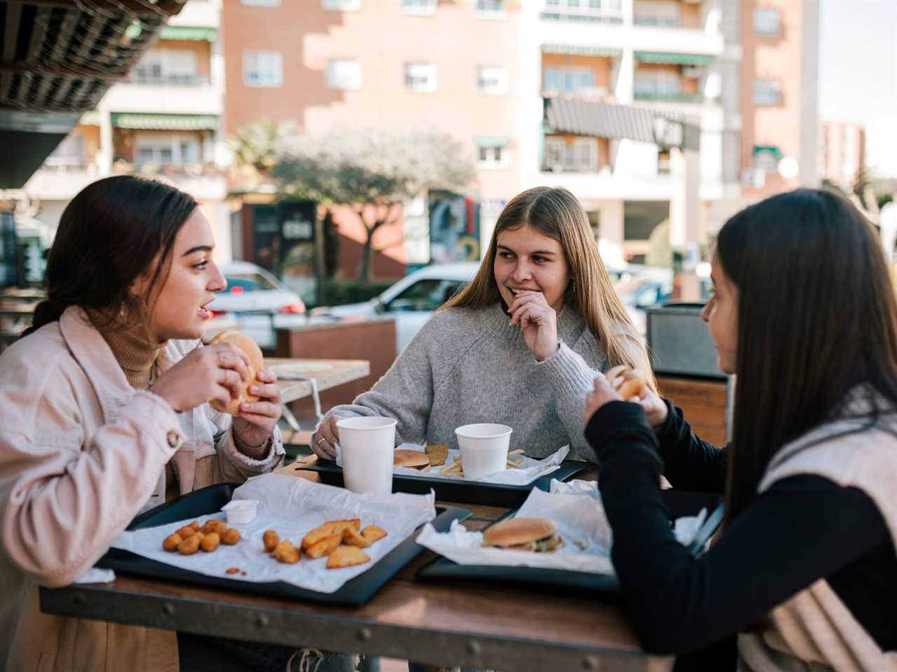 Group of Gen Z teenagers drinking and eating food together sat outside