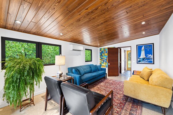 The bright-yellow entrance opens up to the home's main living room, where crisp white walls pop against the original wooden ceiling.