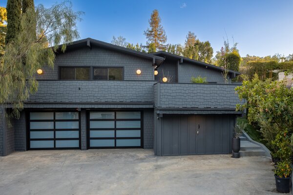 Sporting a handsome gray facade, the shingled home sits perched on a private lot, bordered with lush vegetation. A large balcony awaits on the upper level above the three-car garage.