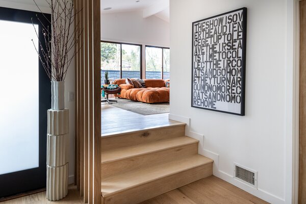 Upon entry, honey-hued wooden steps lead to the home's light-filled living room.