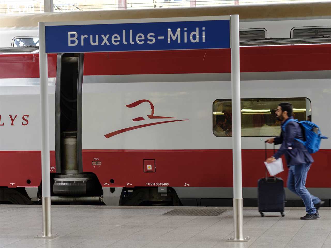 A passenger walking with luggage past a Thalys train at Brussels station.