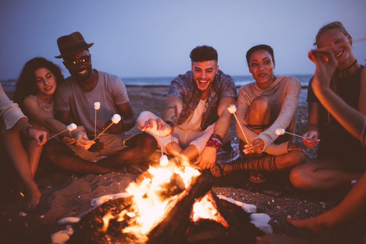 Young friends roasting marshmallows on sticks at the beach