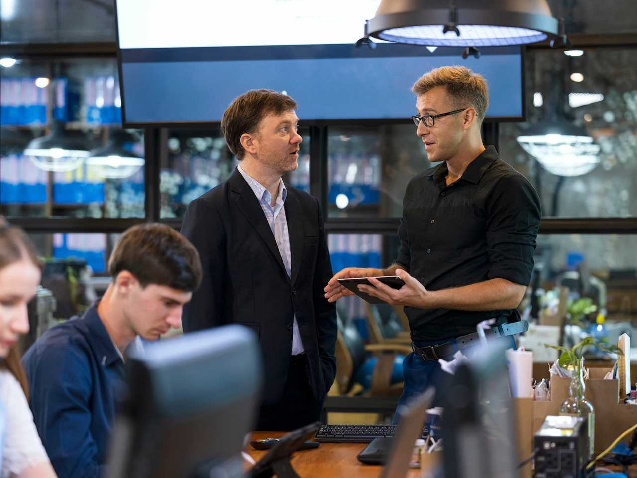 Two people talking in an office while two other people work near them