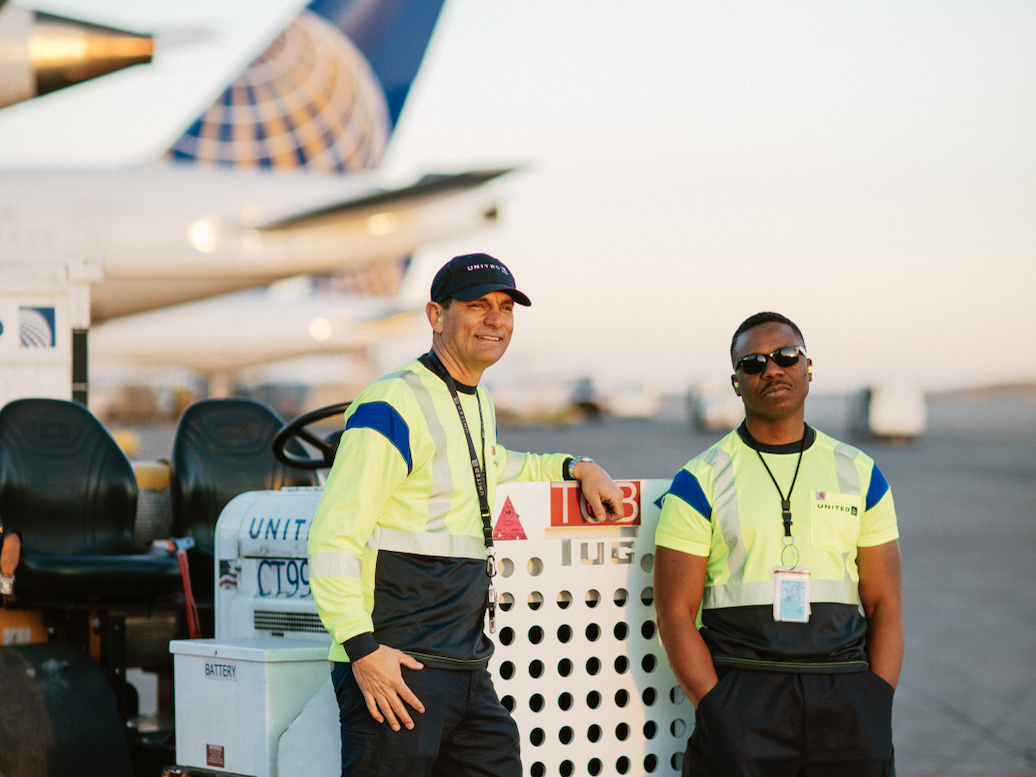 Two United ramp agents wearing the new uniform and standing next to a plane.