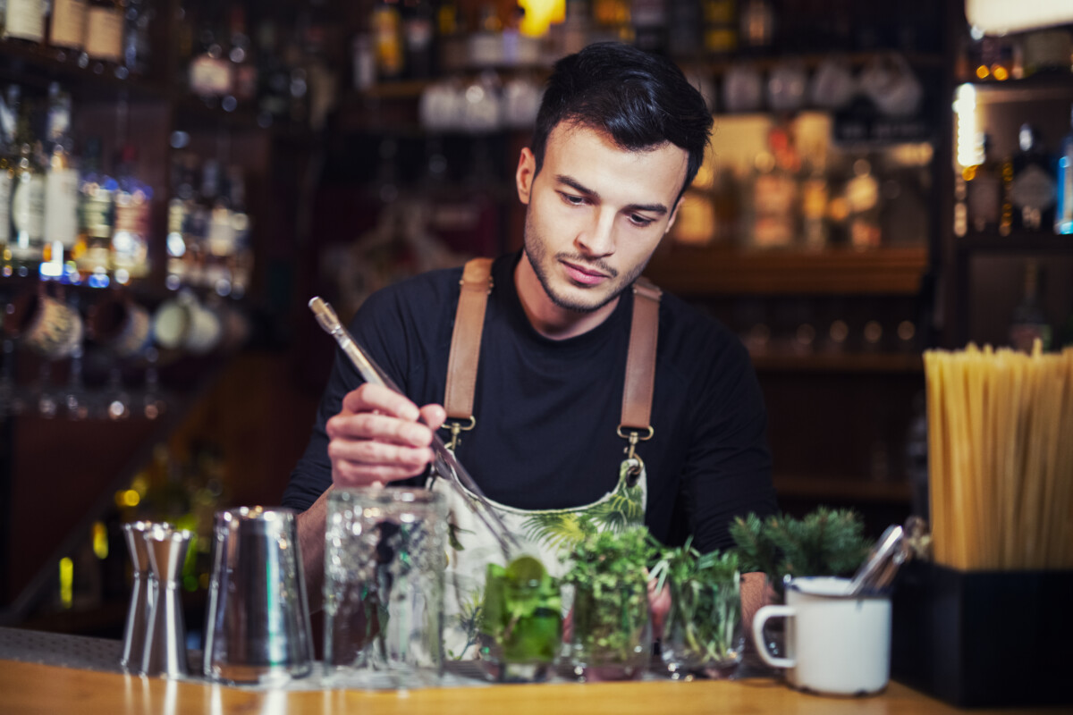 Bartender at bar counter preparing green fresh herbs for next cocktail.