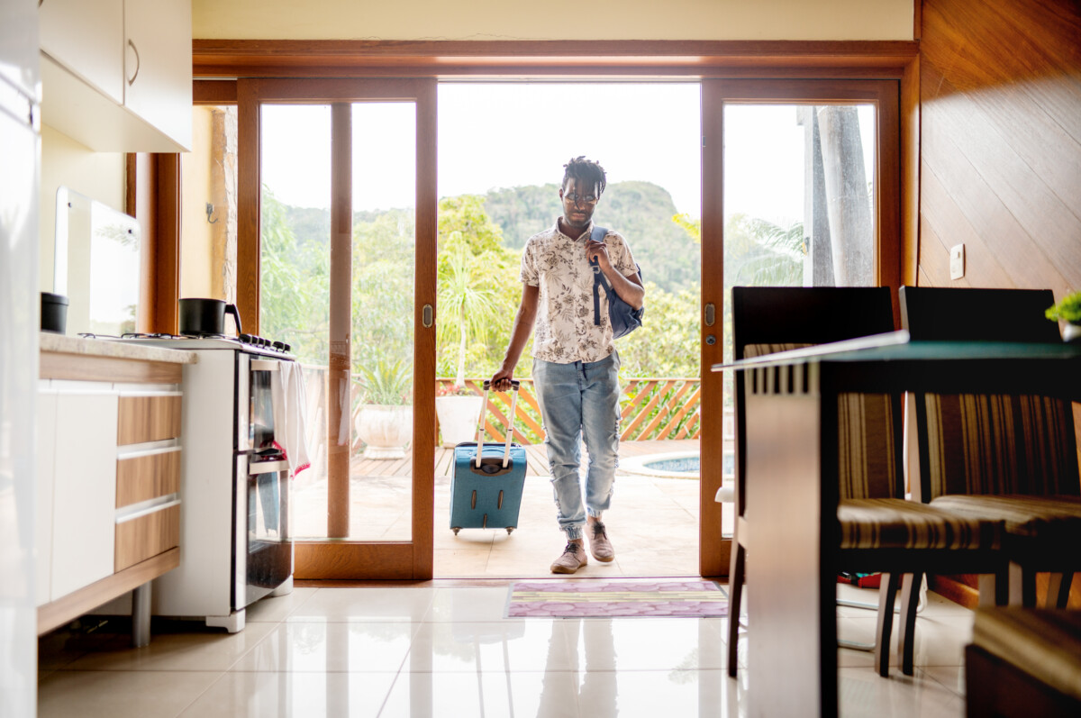 man walking through the patio doors of his rental accommodation pulling a wheeled suitcase