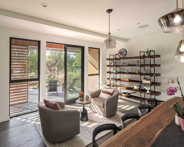 The glazed entrance leads to a small sitting room in front of the dining area. Interior Designer Jennifer Runkle has furnished the space with a focus on neutral colors and natural materials—including a live-edge timber dining table and hanging timber shelves.