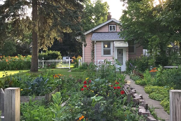 A thriving garden filled with colorful flowers complements the home's blush-pink facade.