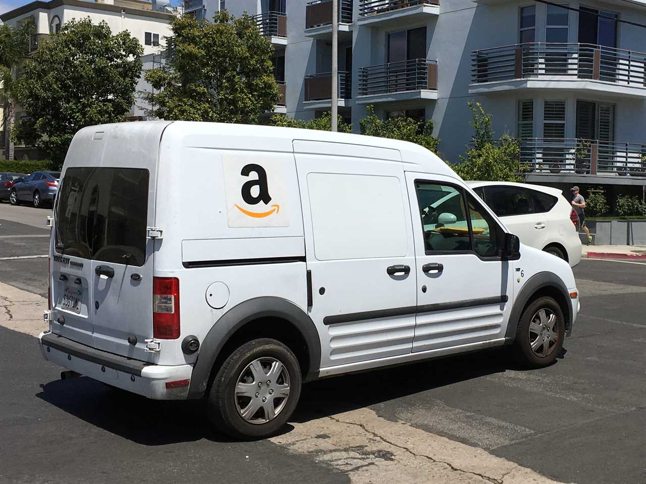 A white Amazon delivery truck sits in a parking lot in front of a building.