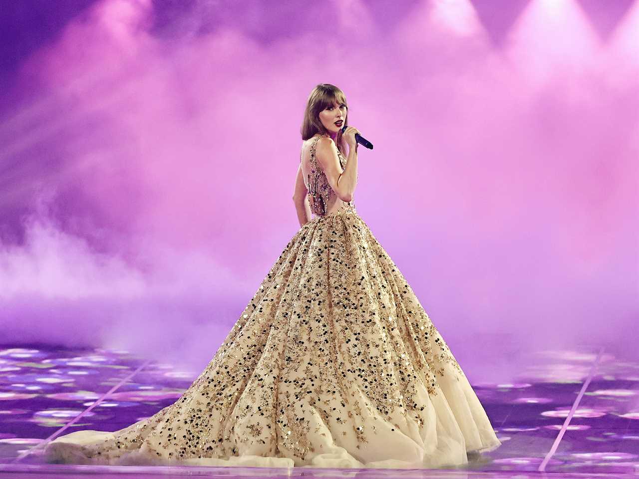 Taylor Swift performs onstage during the Eras Tour wearing a sparkly gold ball gown.