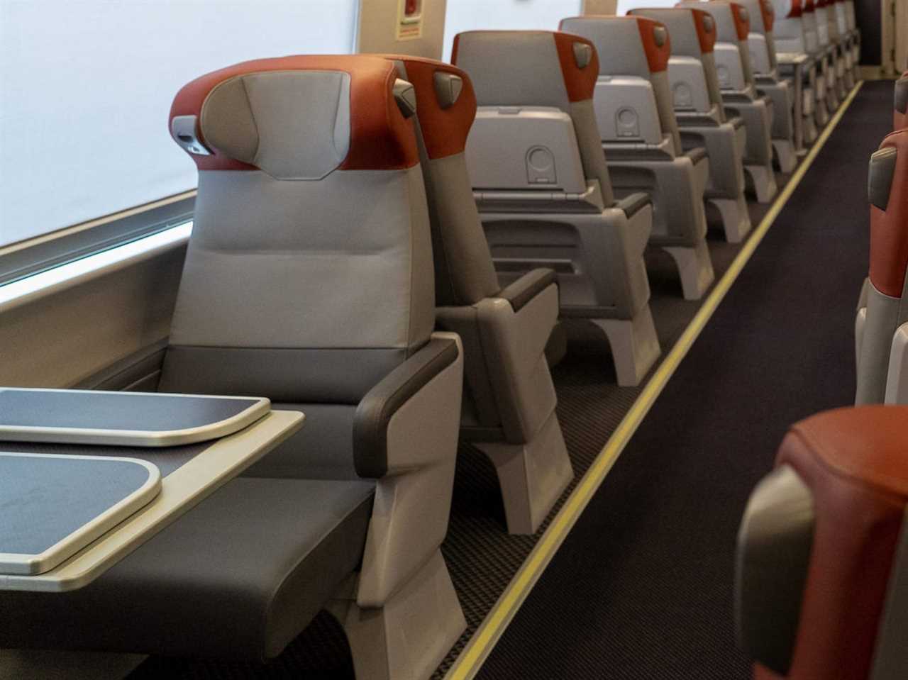 The new Amtrak Acela first class interior with rows of seats with orange headrests and a digital screen.