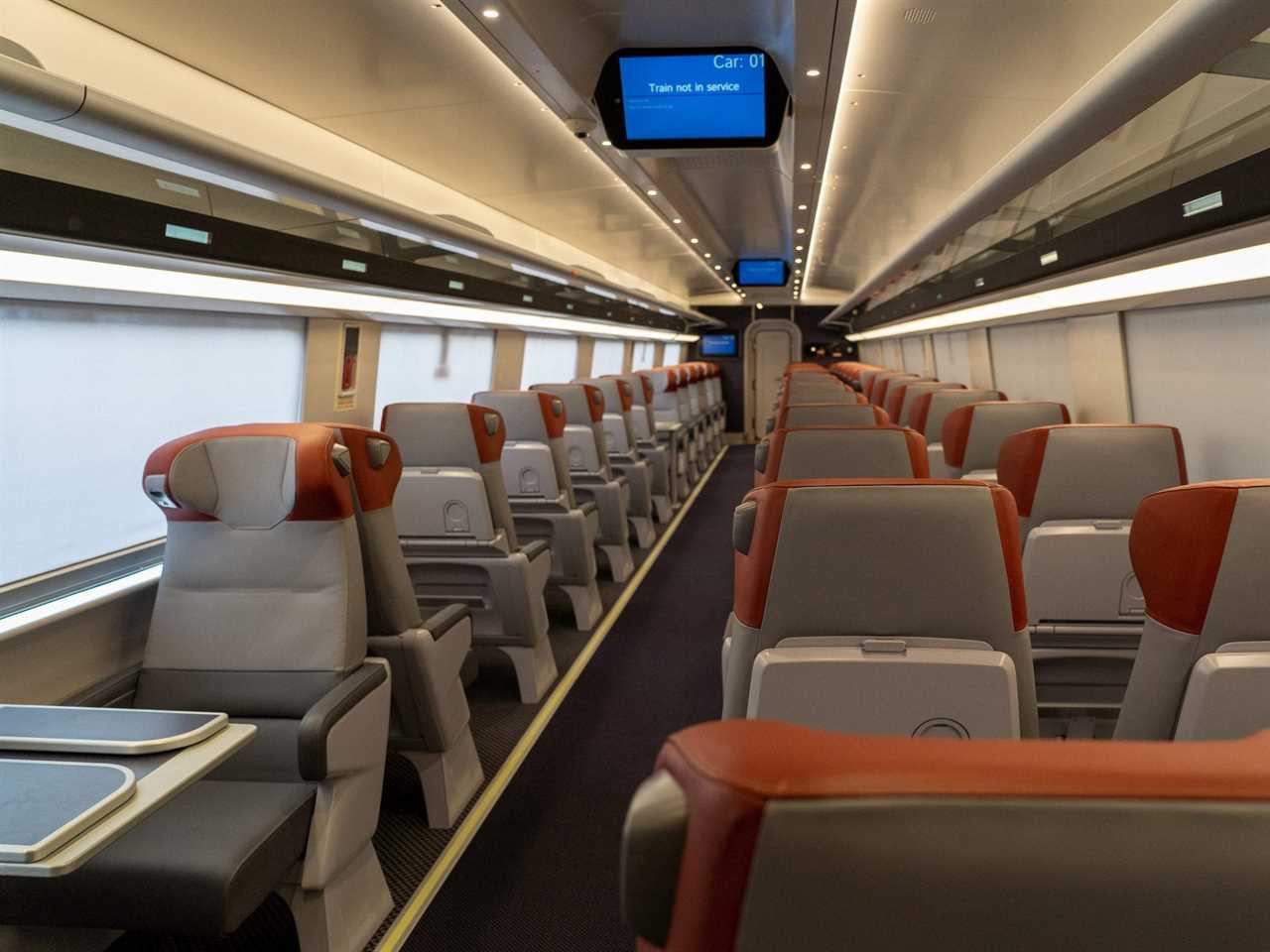 The new Amtrak Acela first class interior with rows of seats with orange headrests and a digital screen.