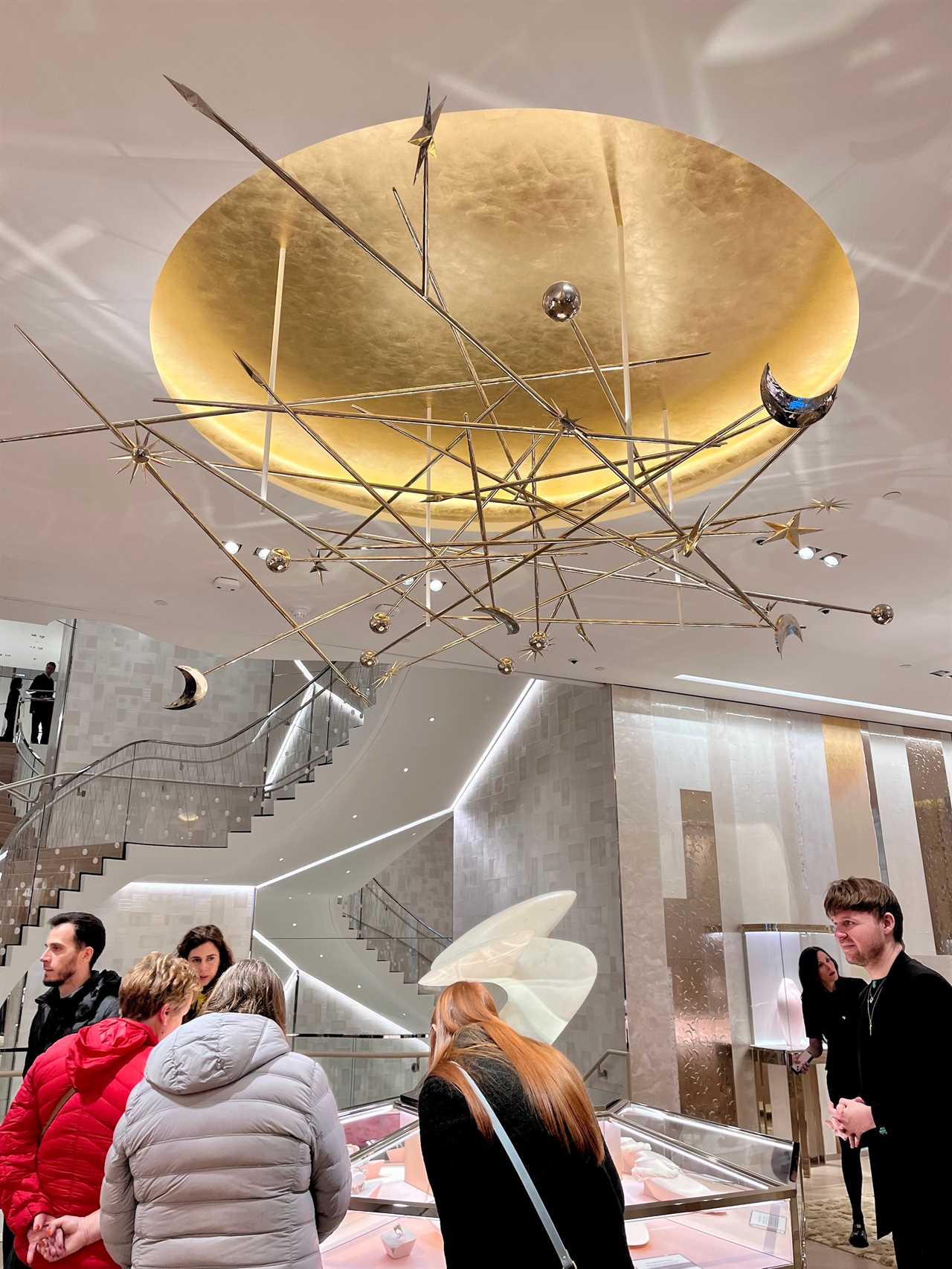 Gold chandelier with stars and moons hangs on ceiling above customers at Tiffany store