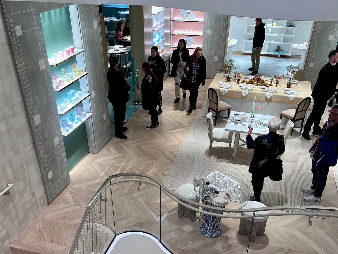 Customers walk around china floor at Tiffany's store next to curved staircase