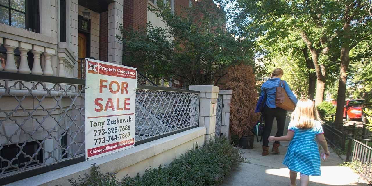 A mother and her daughter walk past a 'for sale' sign.