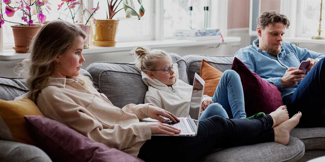 family sitting on couch using laptops and phones