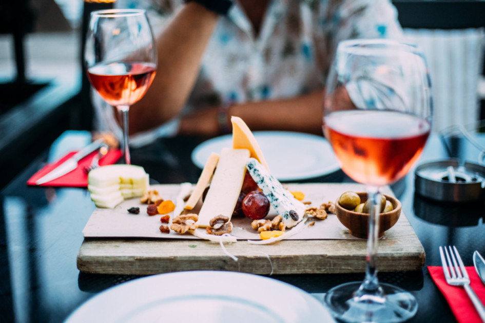 Two glasses of rose wine and board with fruits, bread and cheese on wooden table