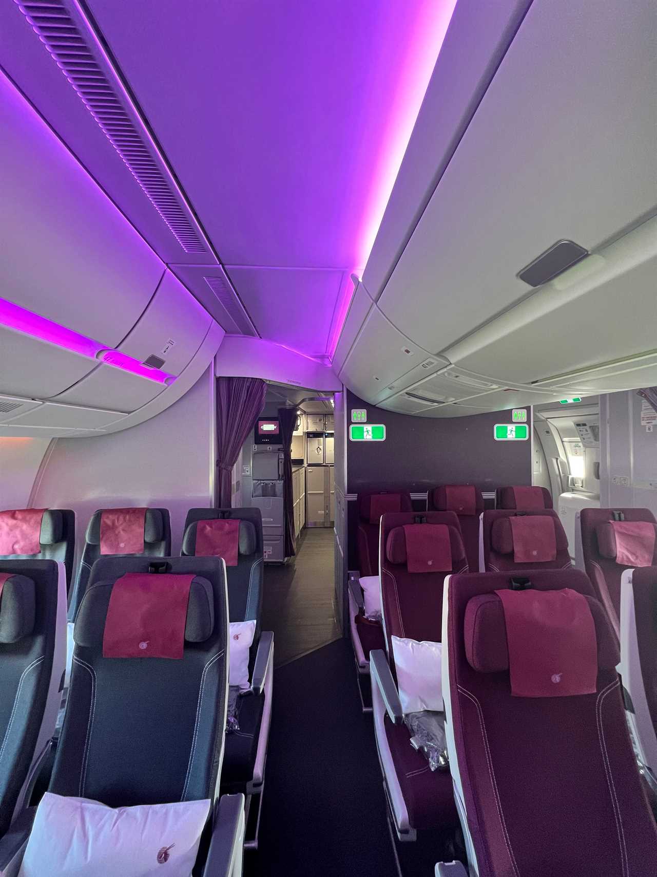 A few economy seats near the back of a Qatar Airways A350 with purple accent lighting, and the galley visible in the back