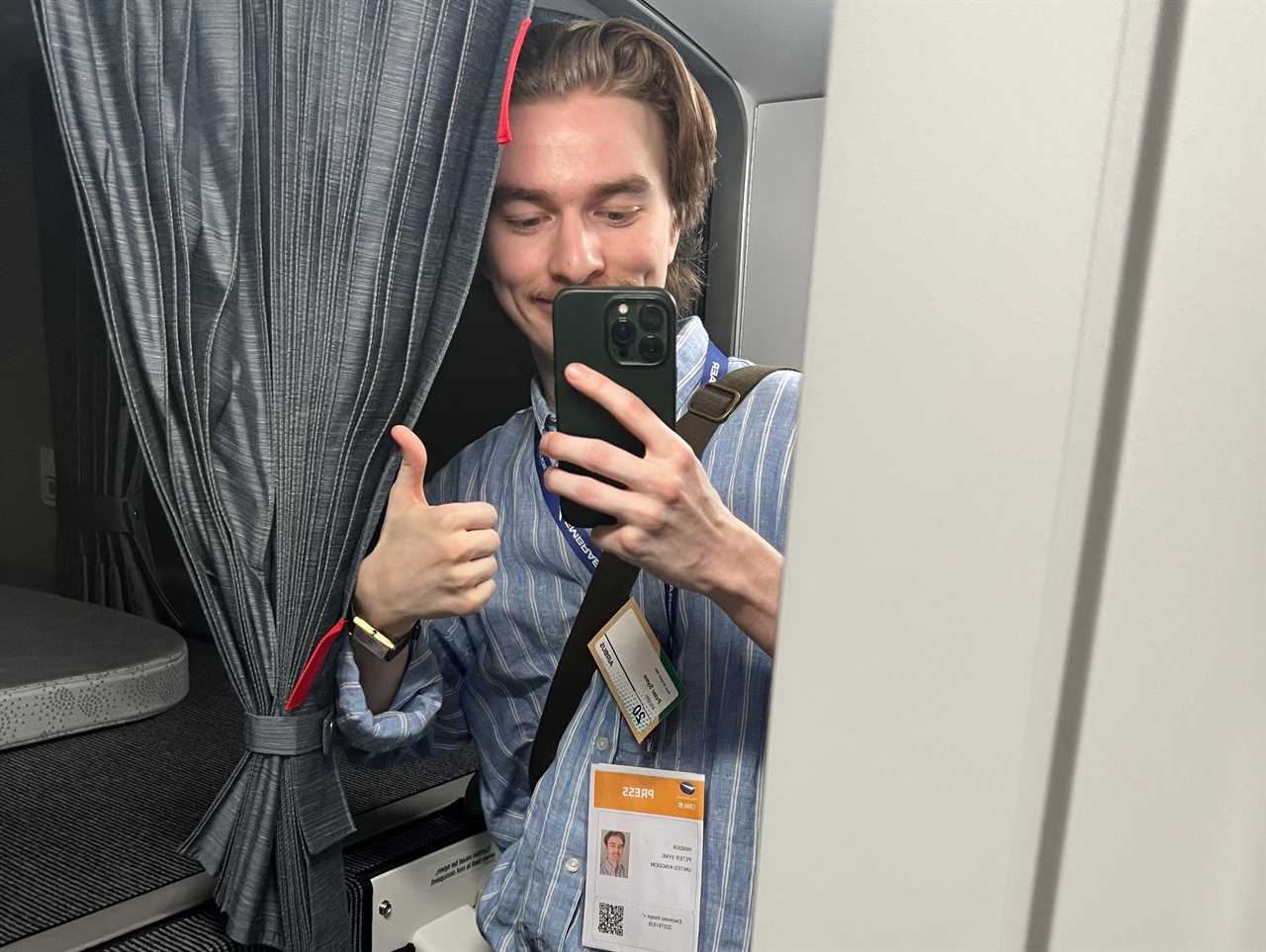 A man in a blue shirt poses with a thumbs-up while taking a mirror selfie in the A350's crew rest area