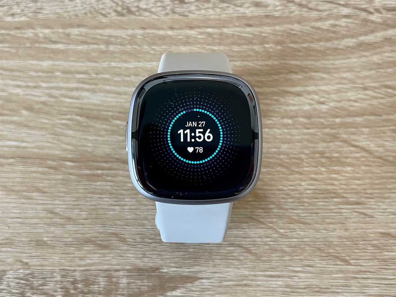 The Fitbit Sense 2 sitting on a wood desk.