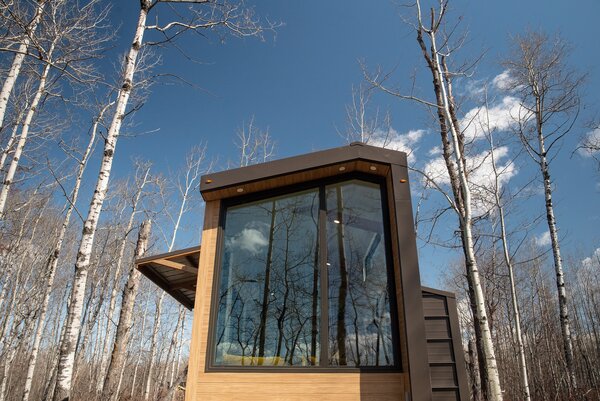 The steel-and-glass wrapped 300-square-foot tiny house that Fritz Tiny Homes designed for Refuge Bay Luxury Camping eco resort in Alberta, Canada, connects to its wooded landscape, providing a feeling of being outdoors while relaxing on the interior.