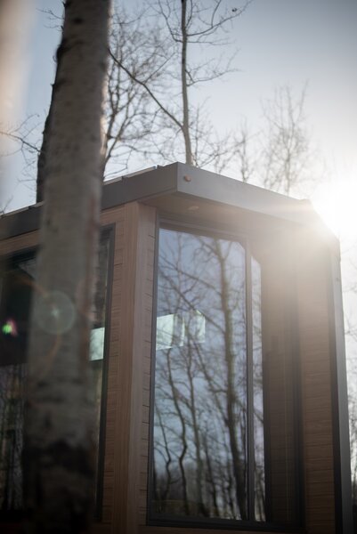 Floor-to-ceiling windows on the front nose of the tiny home blur the line between the interior and the exterior. The wood-printed steel portions of the exterior siding help the accommodation to blend with its forested surround.