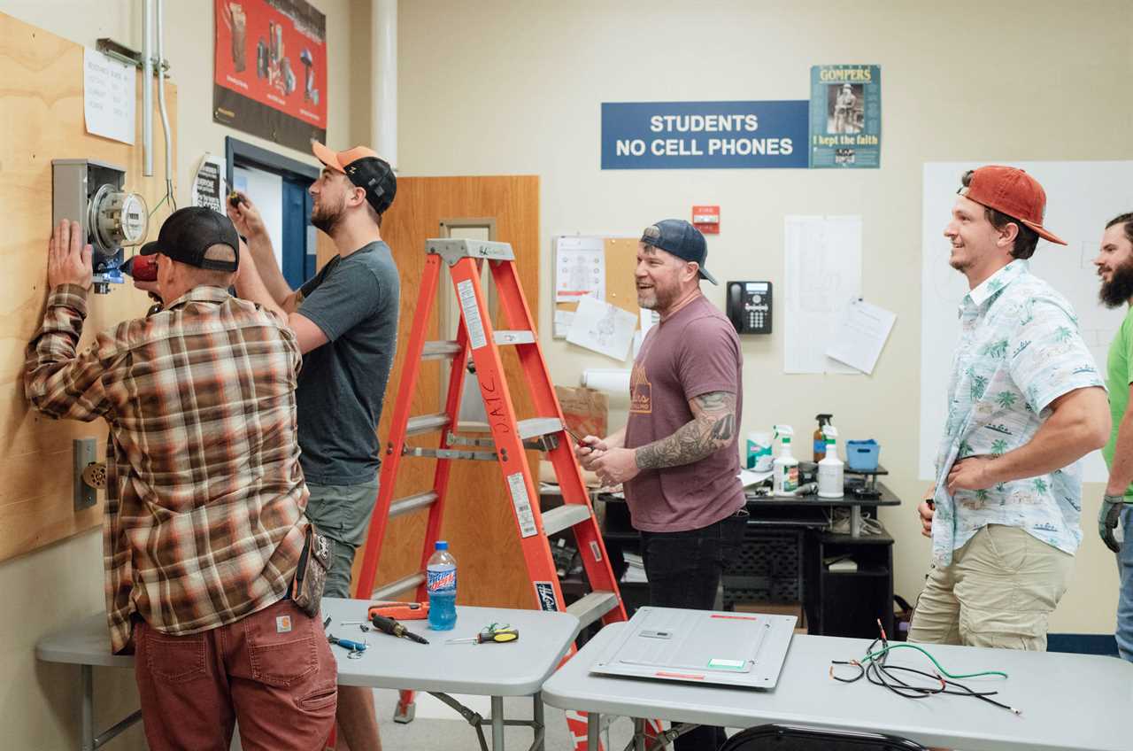 A group of 5 men work installing an electric meter in a classroom.