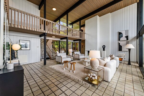 In the double-height living room, floor-to-ceiling windows and a tall brick fireplace enhance the home's grand sense of space.