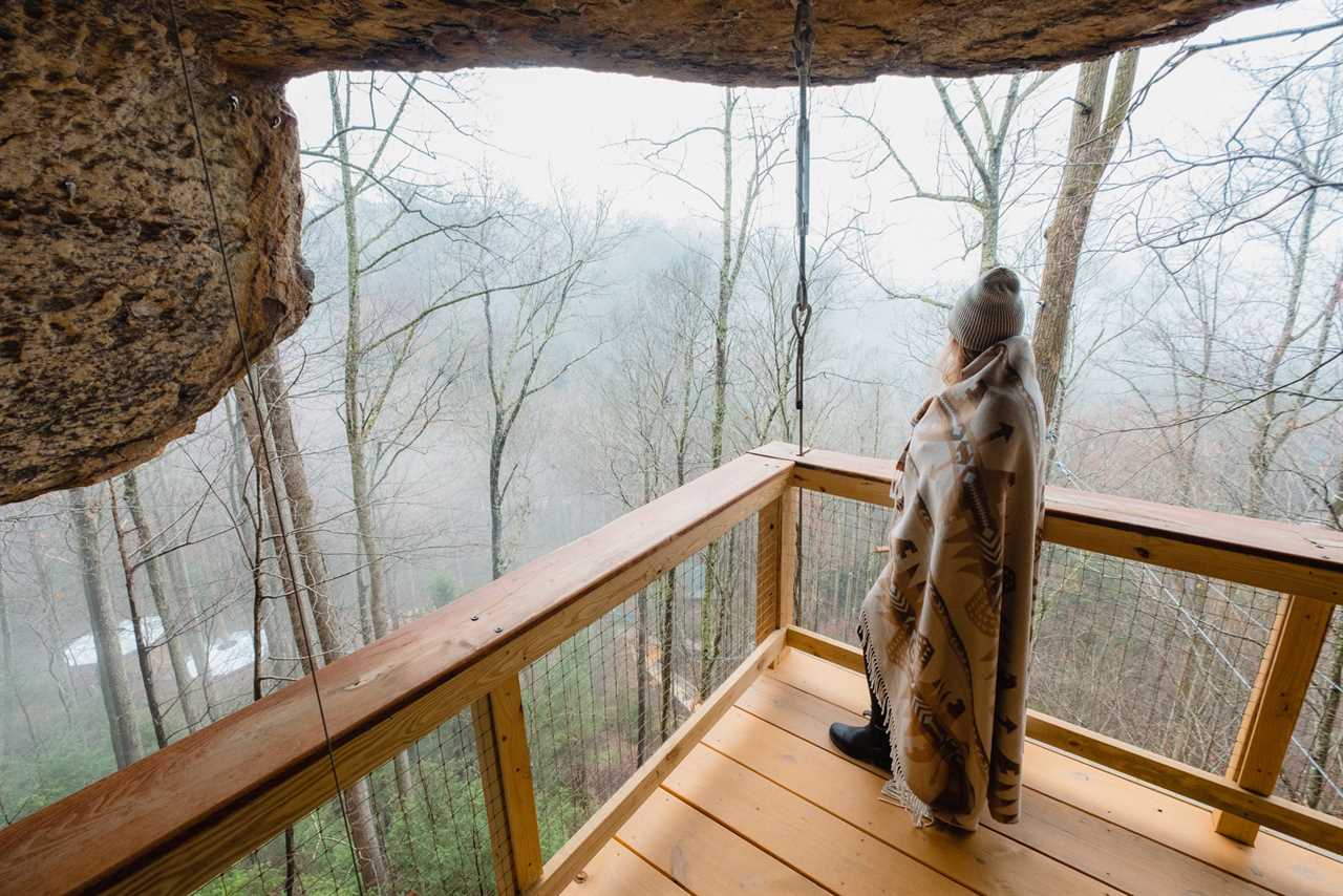 A person at Cliff Dweller looking over a forest from a treehouse deck.