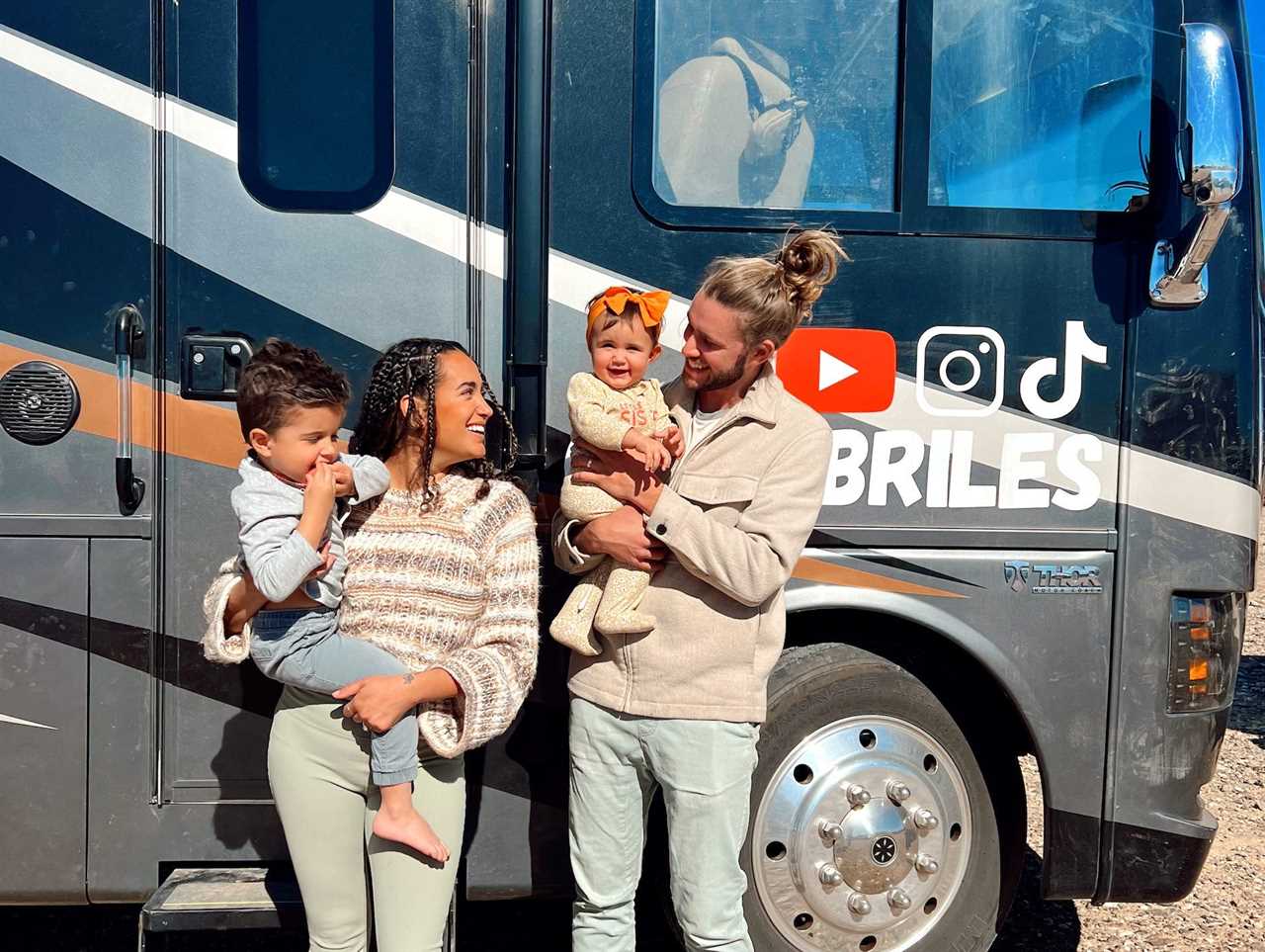 A husband and wife holding their children in front of an RV