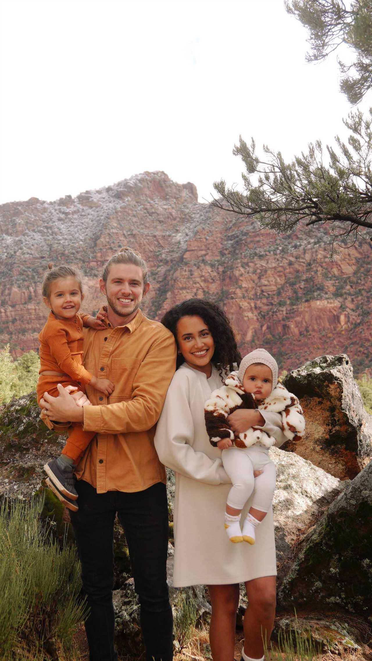 A man and woman holding their young children in front of a mountain.