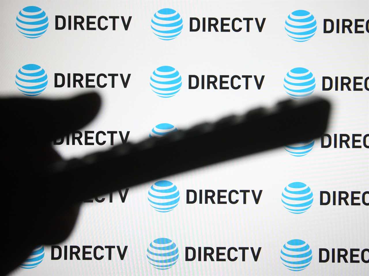 Shadow of a person using a phone in front of a background with DirecTV logos