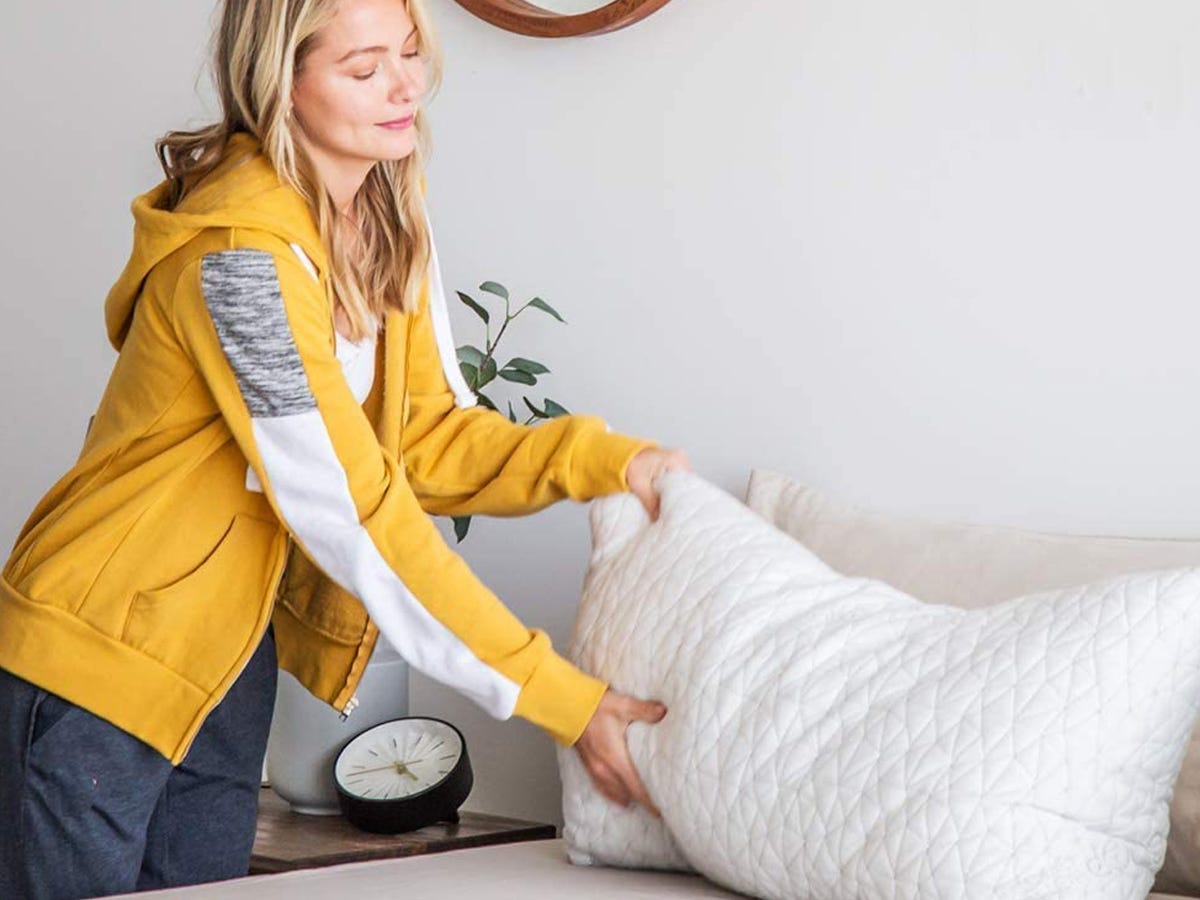 person placing large white pillow on a bed