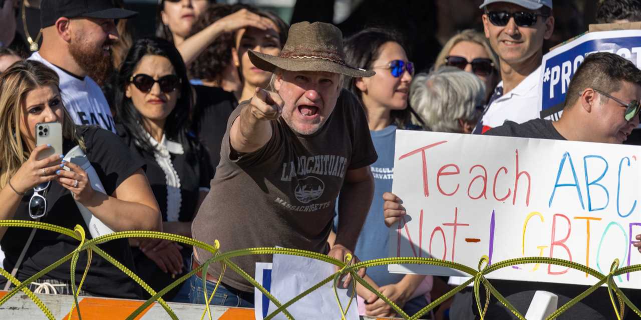 enraged man pointing behind barrier next to sign that says "Teach ABC not LGBTQ"