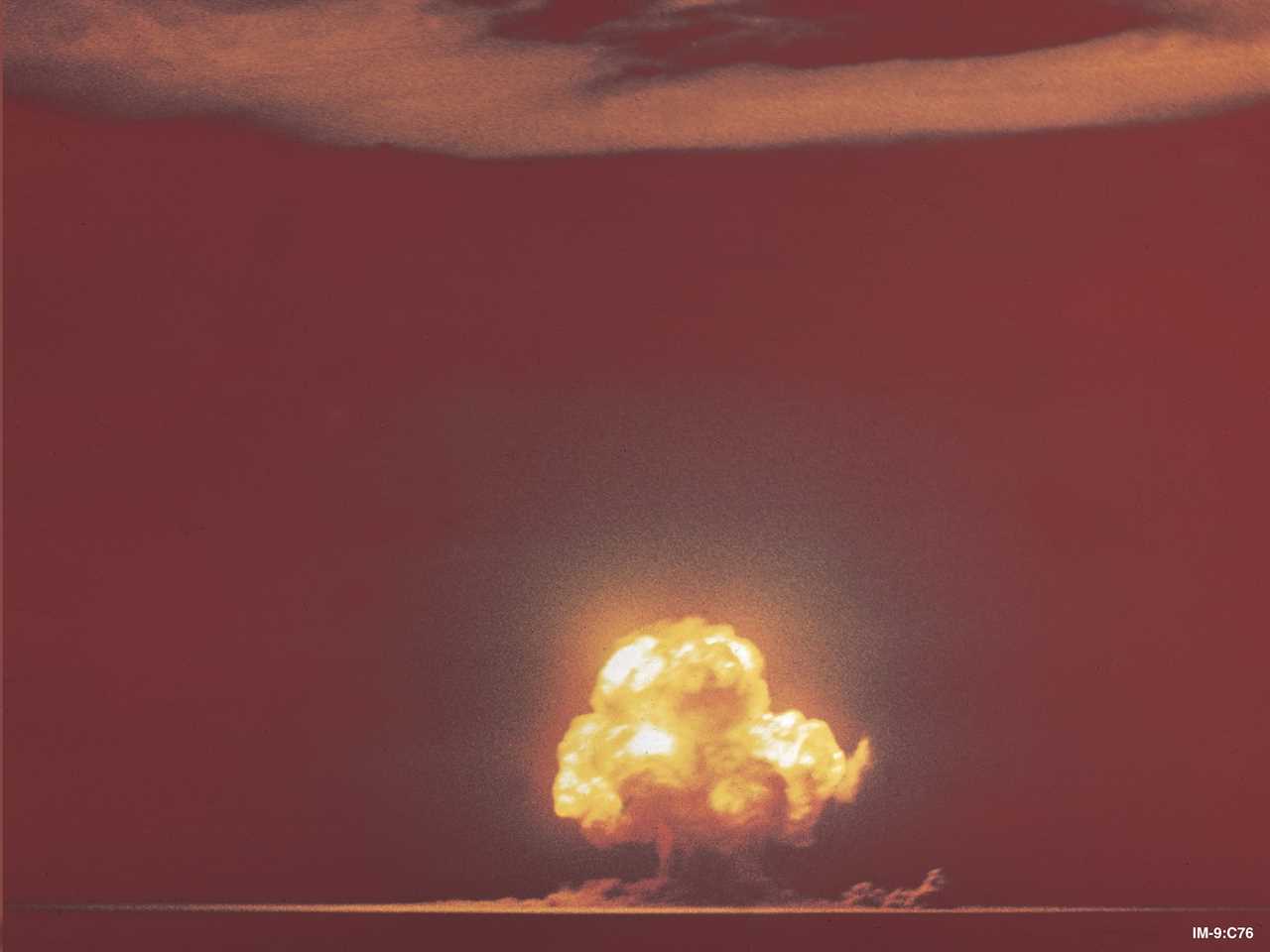 trinity nuclear bomb test distant yellow mushroom cloud erupting into orange sky