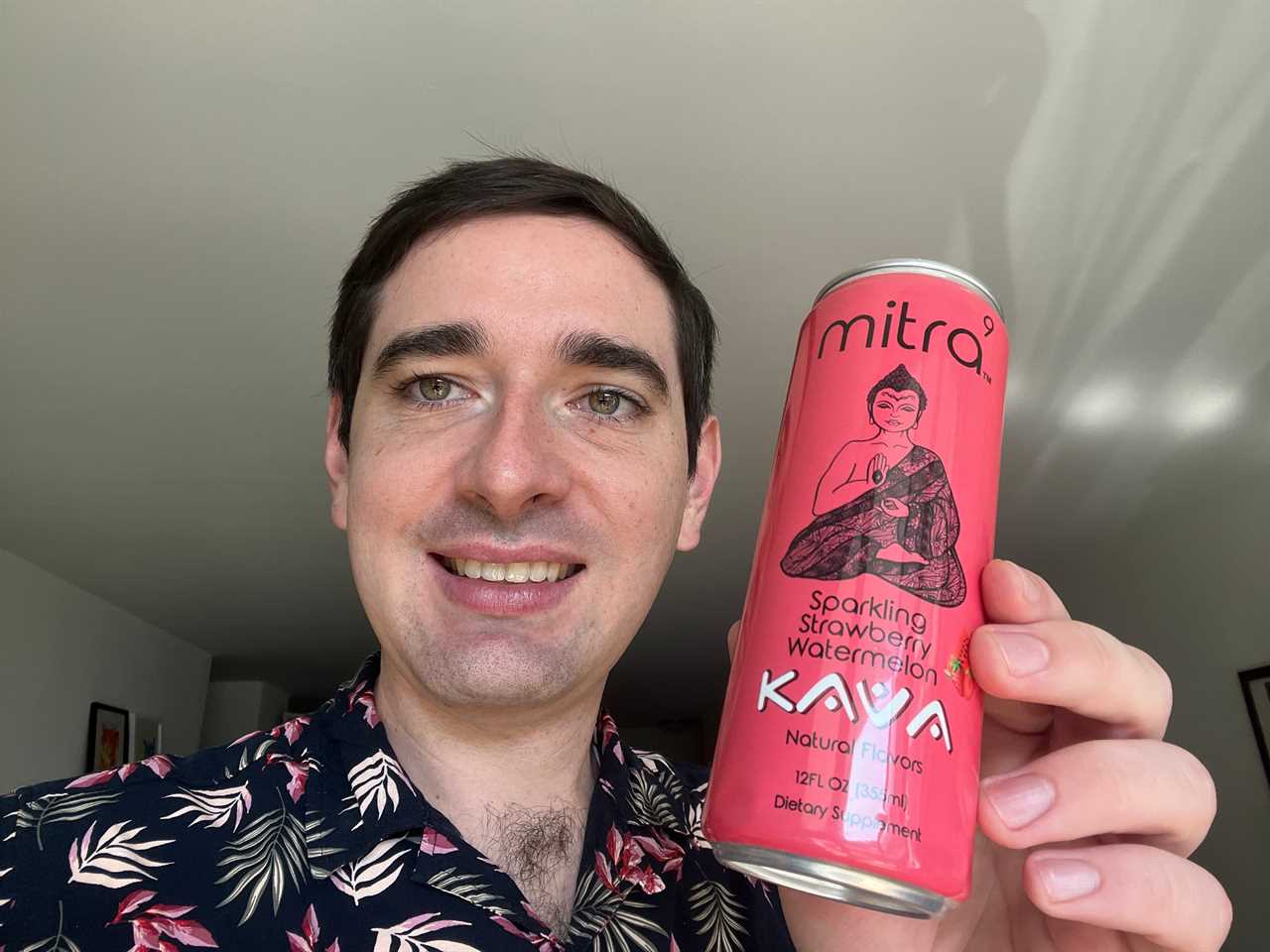 Insider Reporter Alex Bitter holds a can of Mitra-9, a canned kava beverage, while facing the camera and wearing a black floral-print button-up shirt.