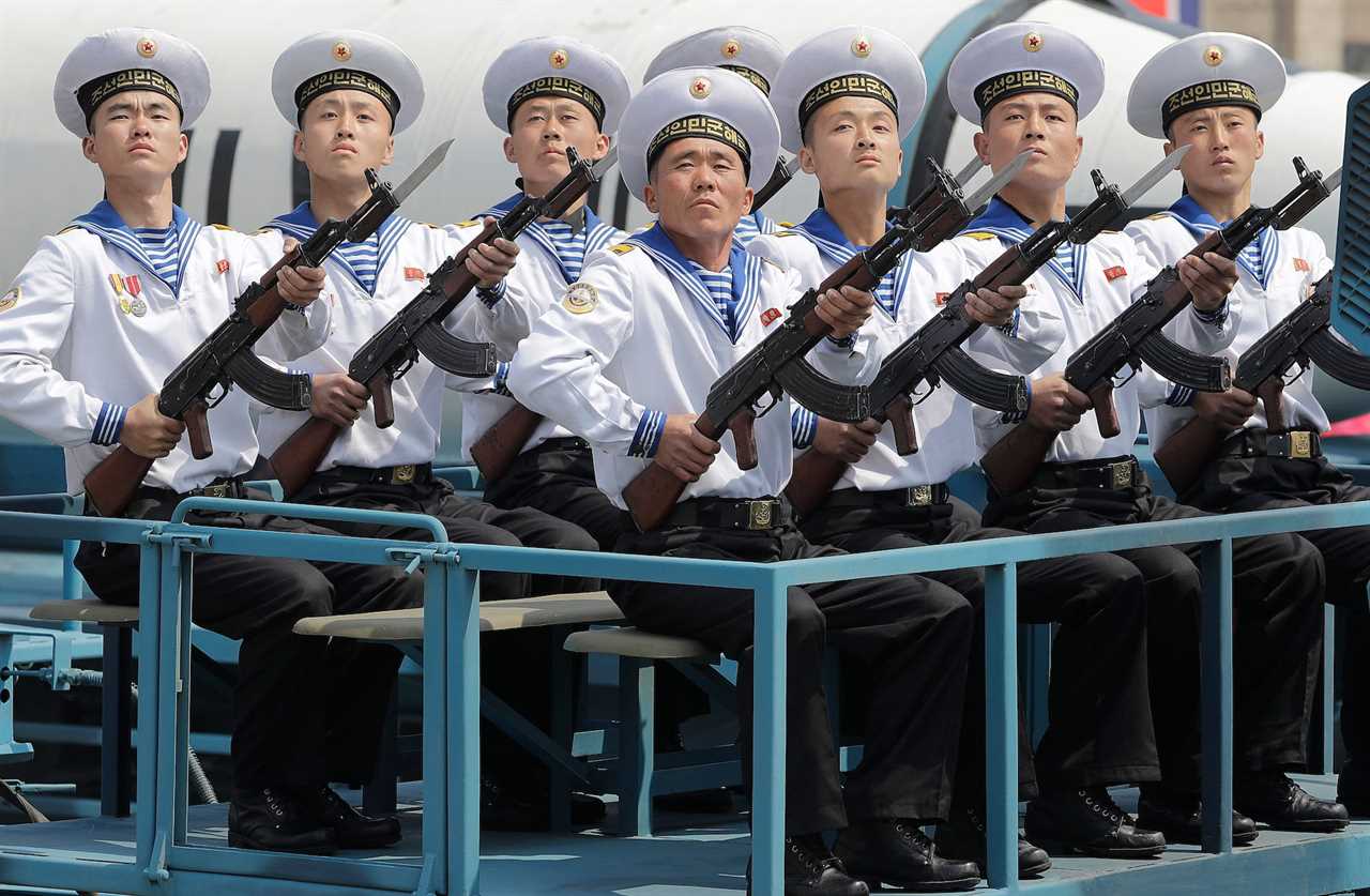 Navy personnel in uniform seated while holding rifles