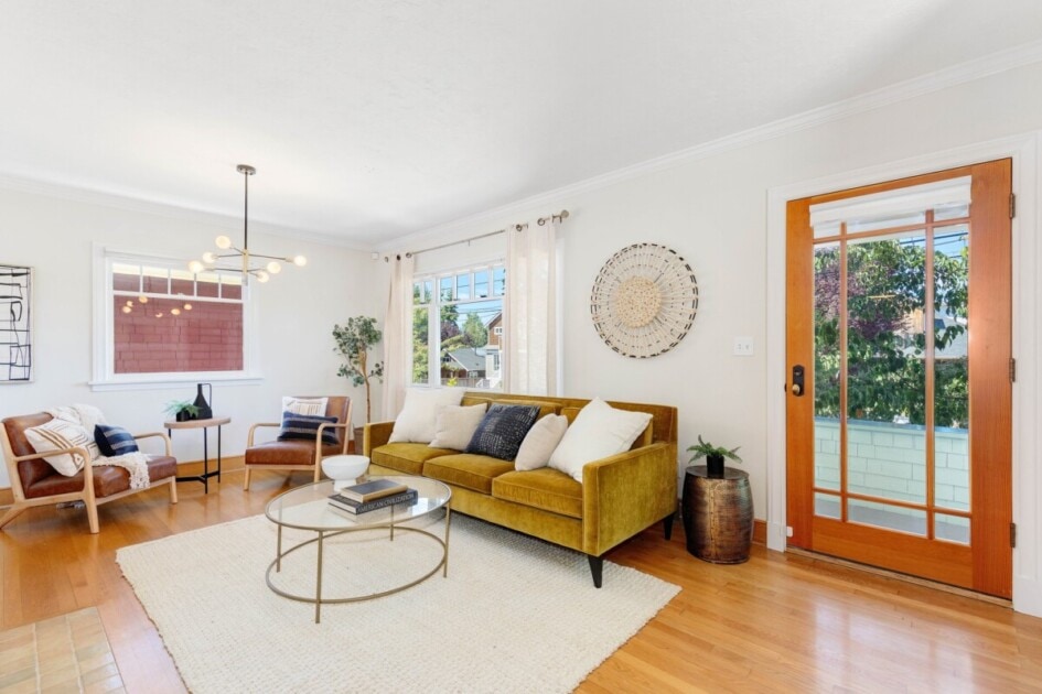 Living room with yellow velvet sofa and area rug over hardwood