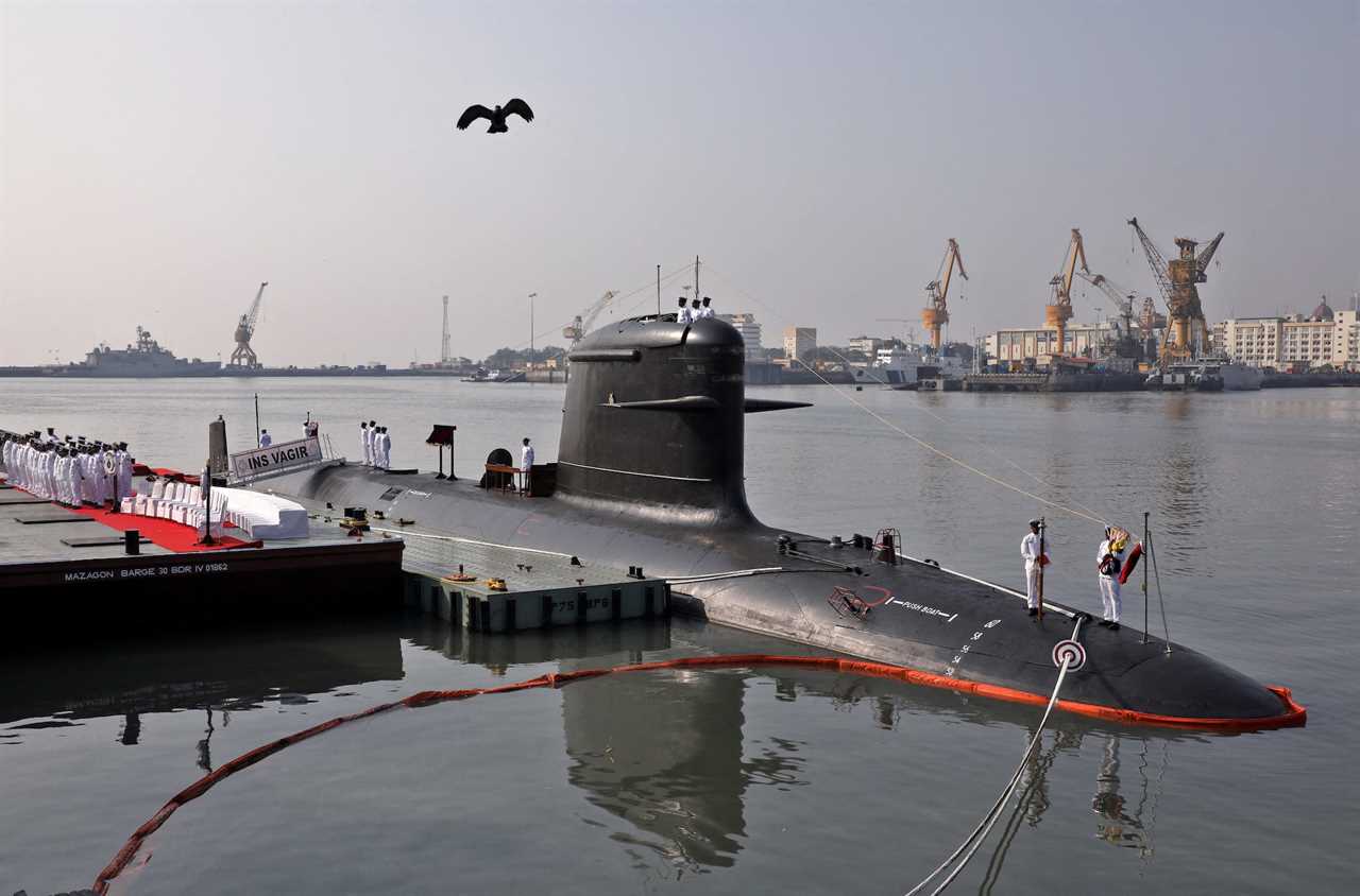 Indian Navy officers stand on a submarine in a dockyard