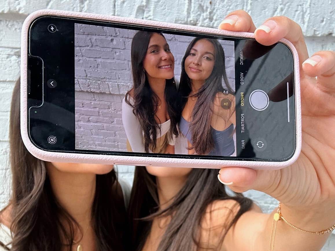 Two girls taking a selfie with a phone in front of them. The phone covers their faces, but their image can be seen on the phone screen.