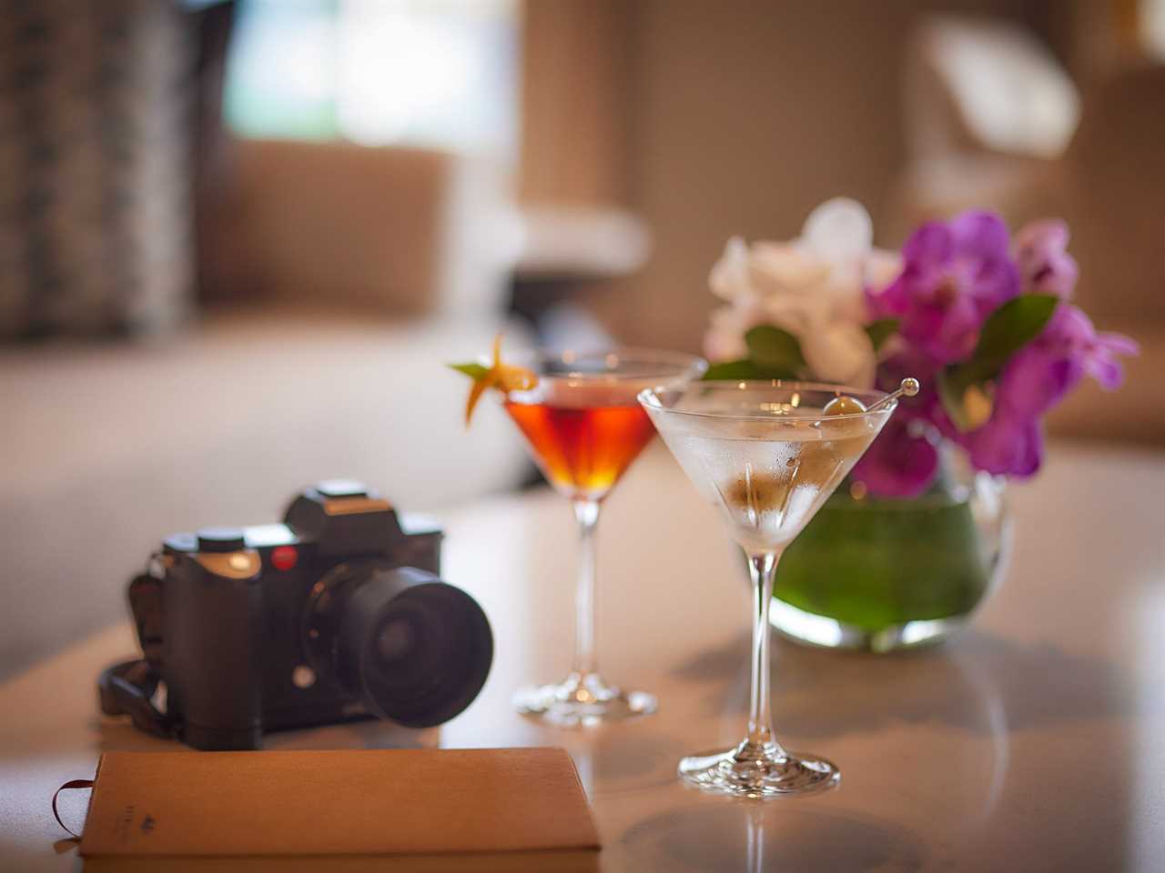 A tabletop where a set of cocktail glasses and a camera have been placed next to a vase of flowers.