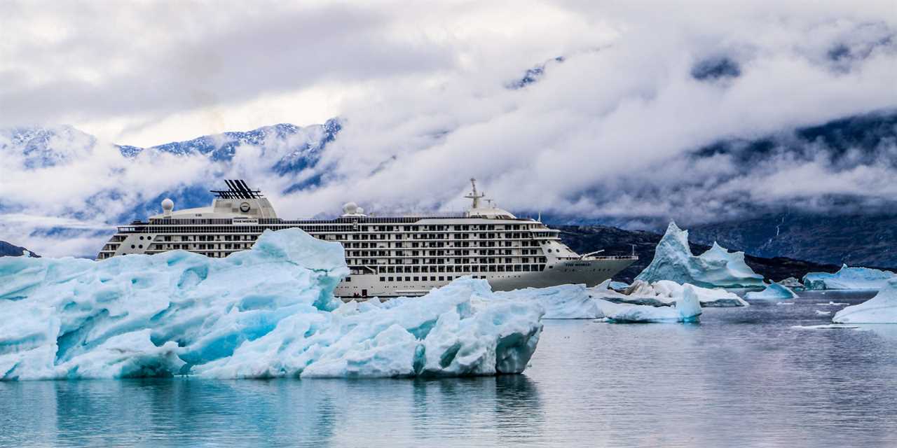 The World sailing past large, jagged-looking icebergs in an icy body of water.