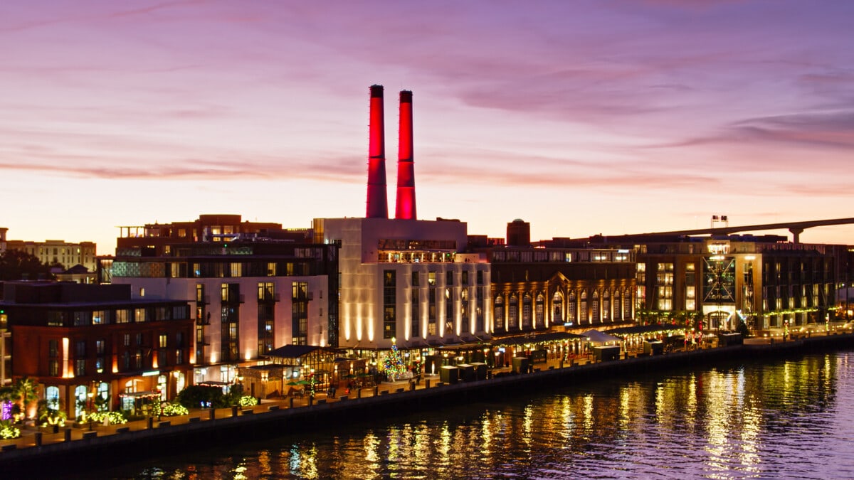 Aerial shot of the historic waterfront of downtown Savannah, Georgia after sunset, with a colorful purple sky reflecting in the water of the river.