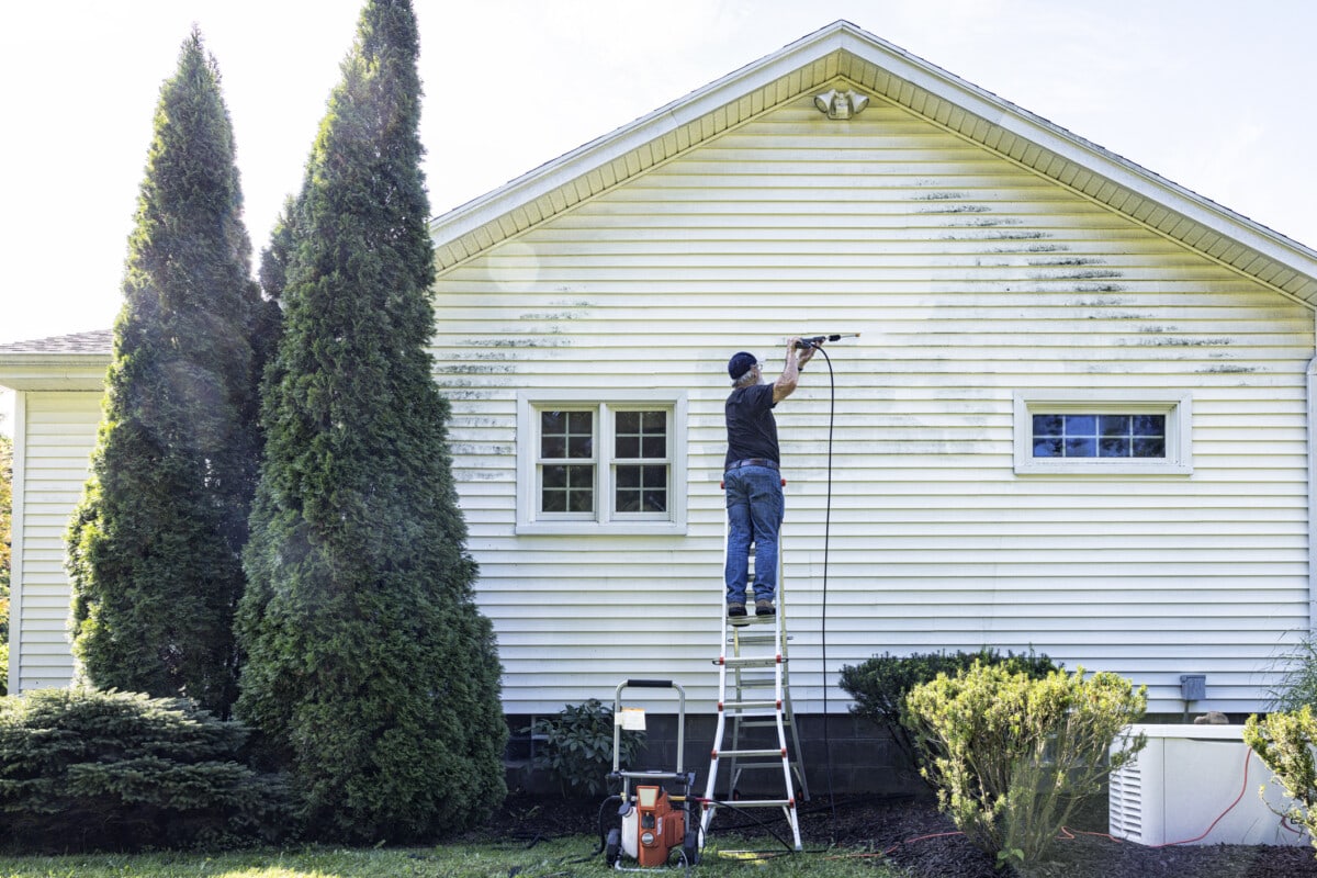 Homeowner pressure washing siding of house