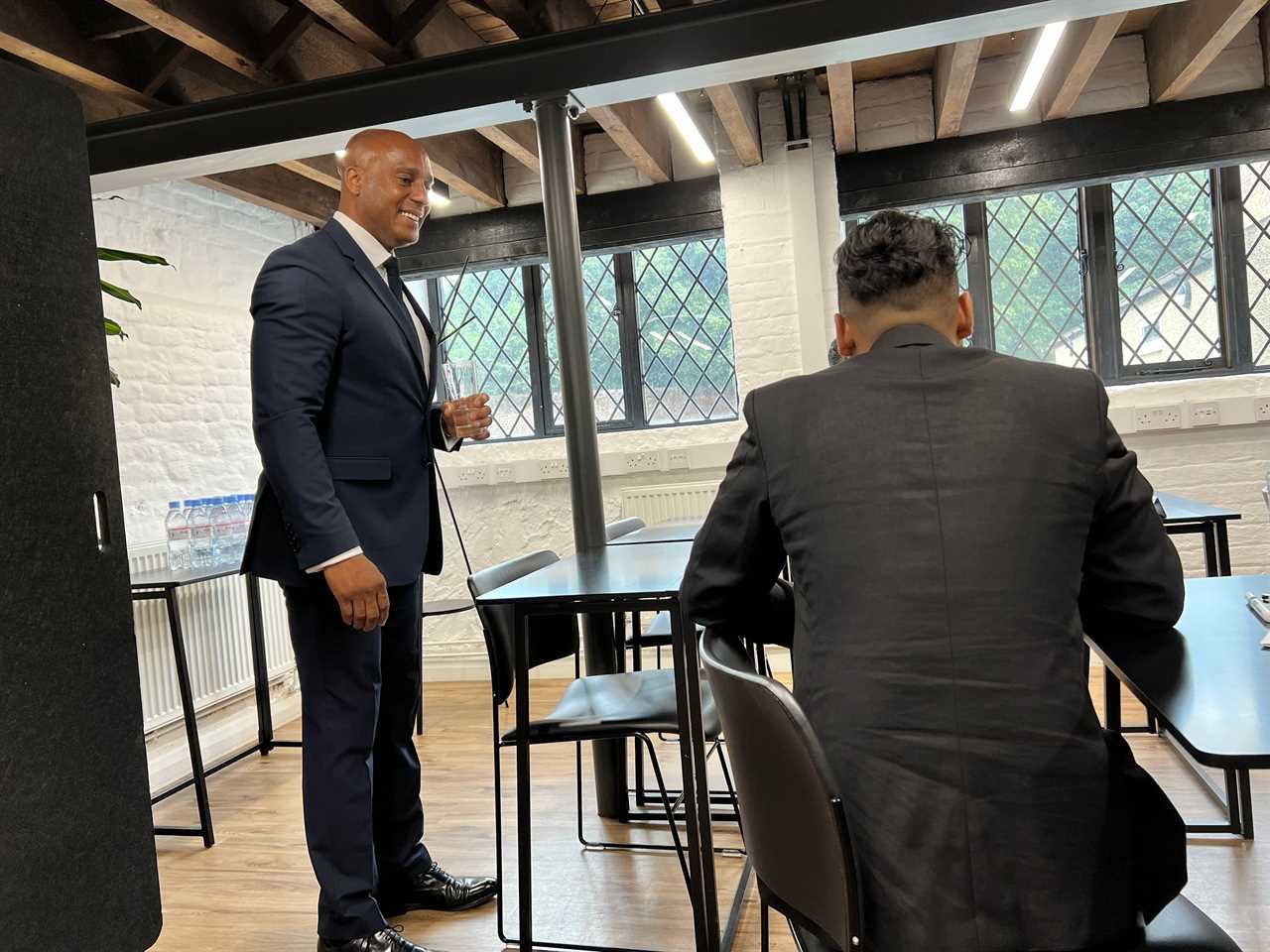 Ricky Miller of Wheely wears a navy suit and smiles while talking to two chauffeurs