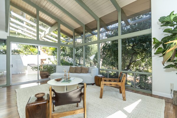 Floor-to-ceiling windows wrap around the main living area, while sliding glass doors extend the room to the partially covered patio.