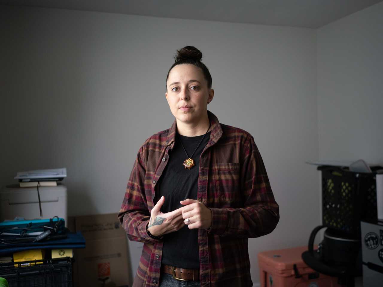 Renee Zinsky in an empty room in a flannel shirt, surrounded by boxes.