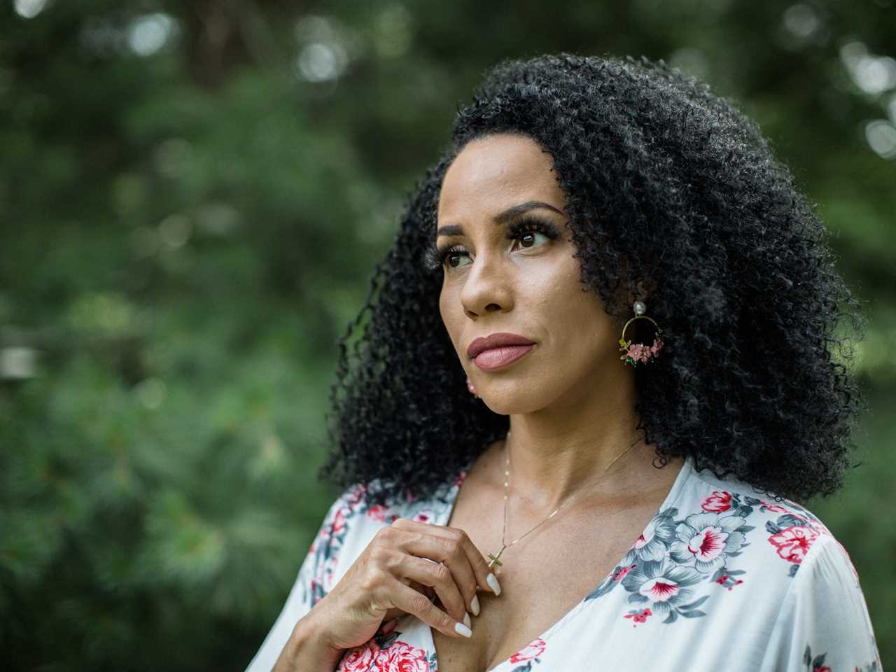 Woman holding a cross on her necklace with trees in the background